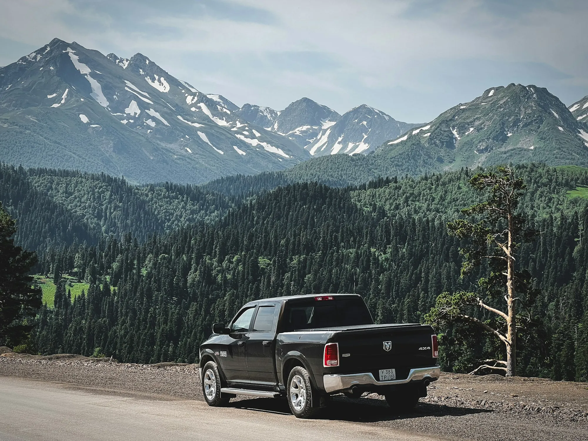 Black pickup truck parked on a gravel pull-off below snowy mountain peaks