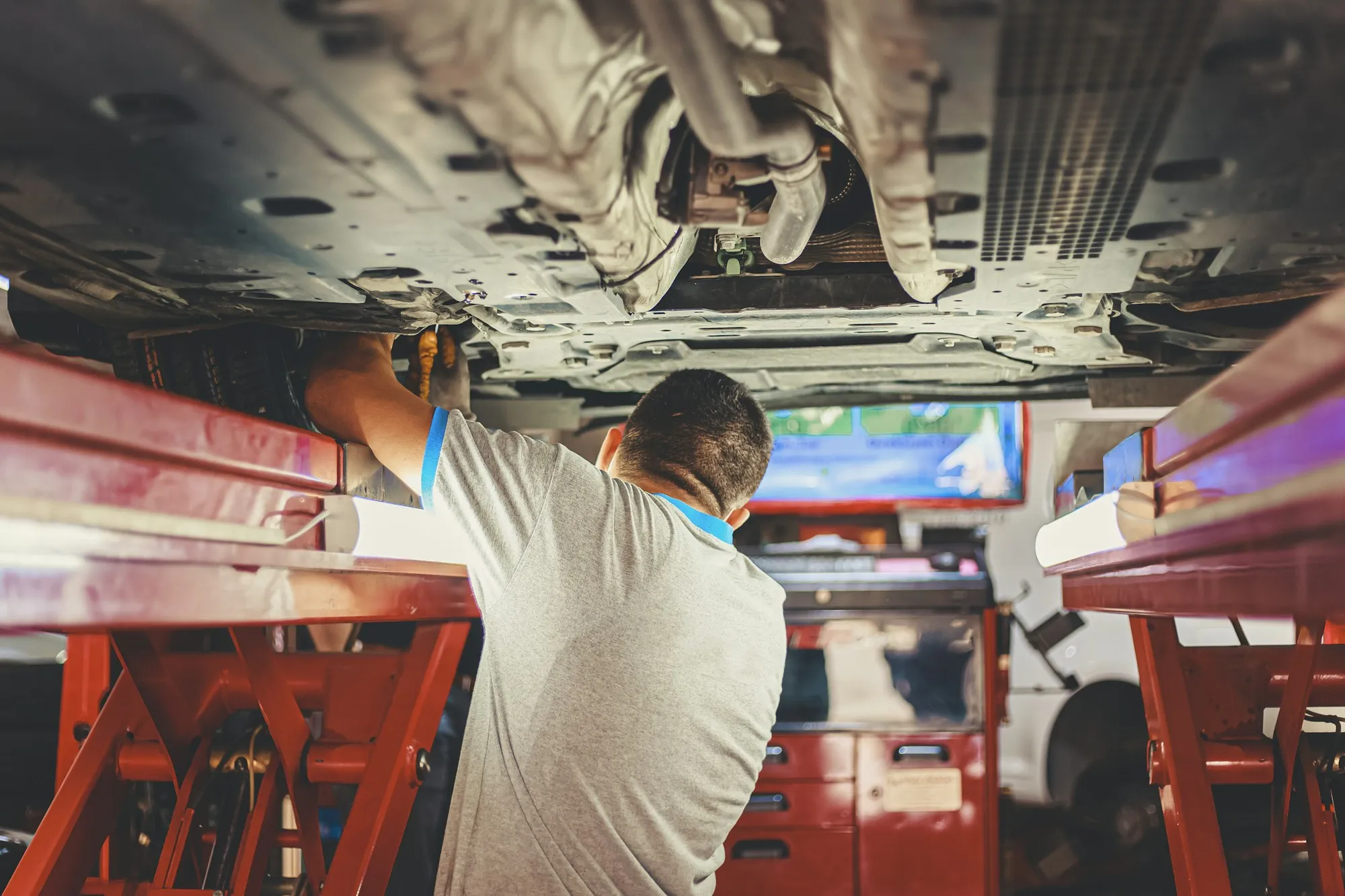 Technician working underneath a vehicle raised on a red lift