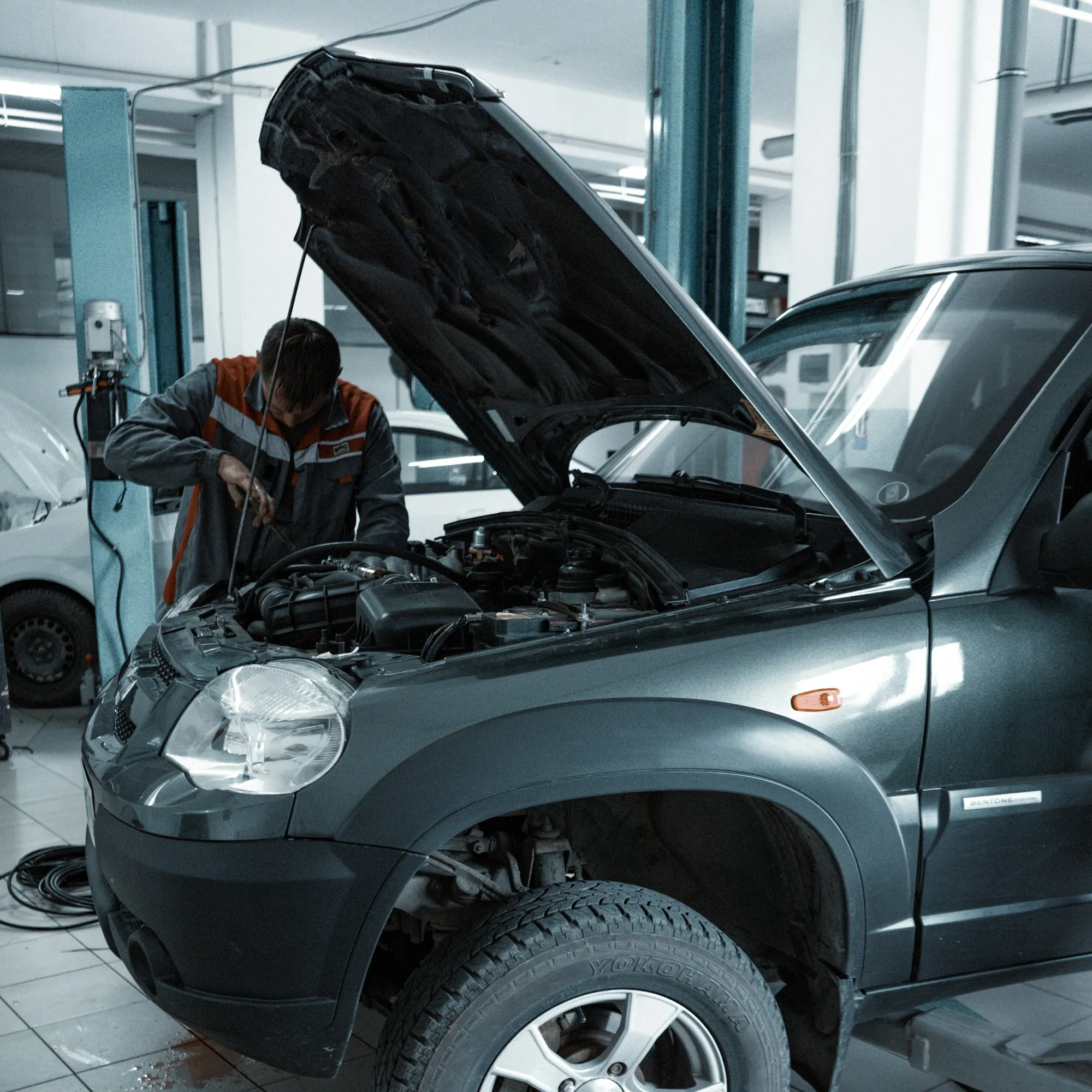 Mechanic leaning into the engine bay of a grey SUV with the hood up