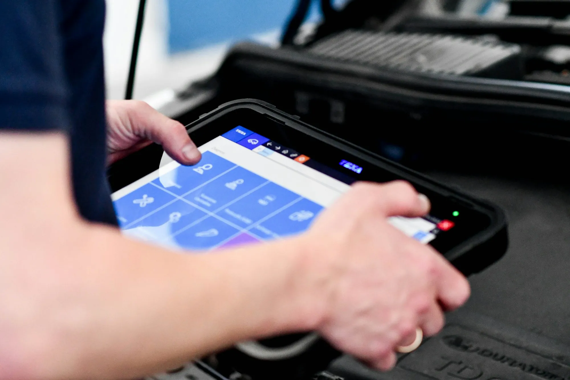 Technician using a handheld diagnostic tablet connected to a vehicle