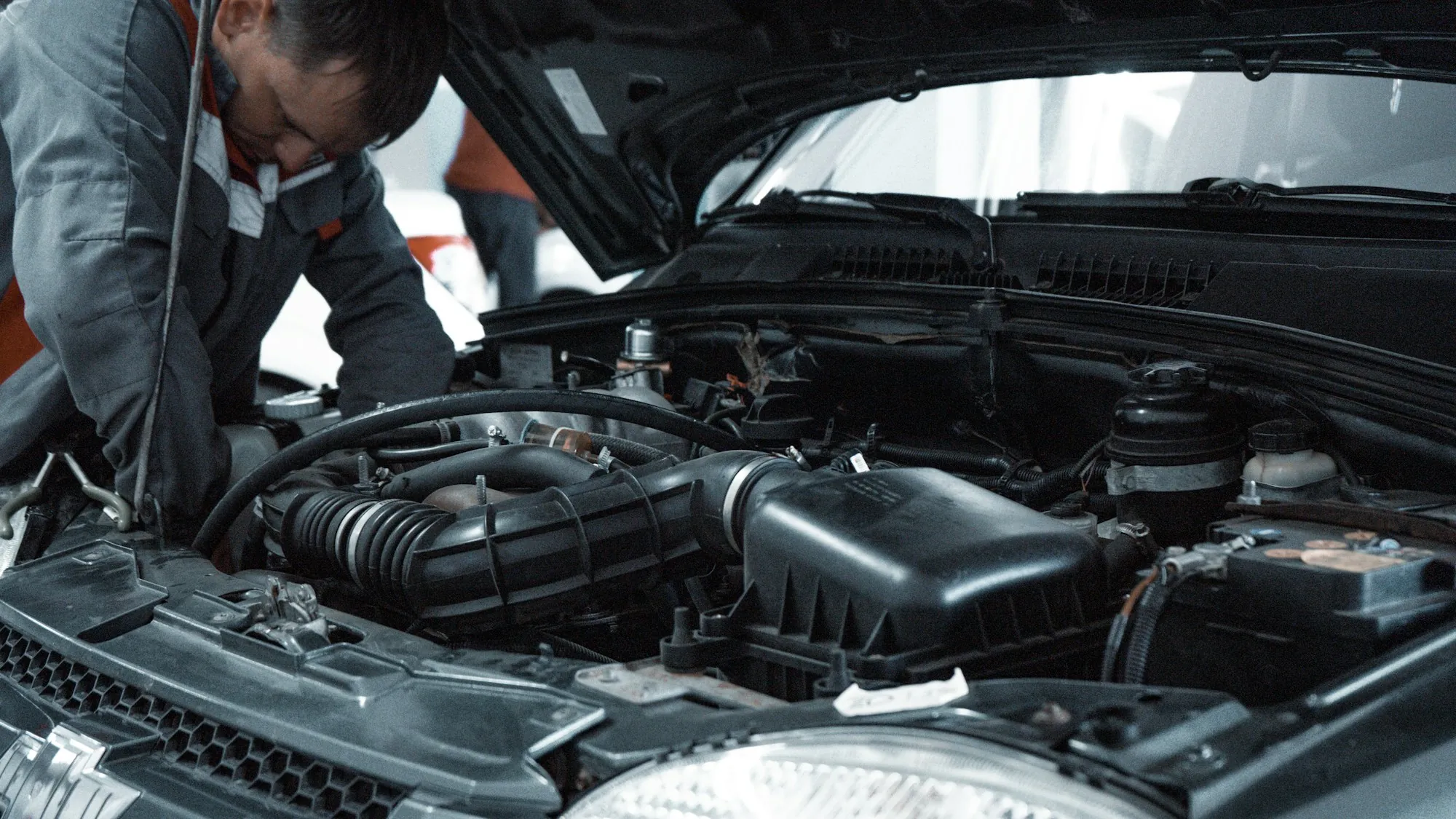 Technician leaning over an open engine bay checking hoses and components