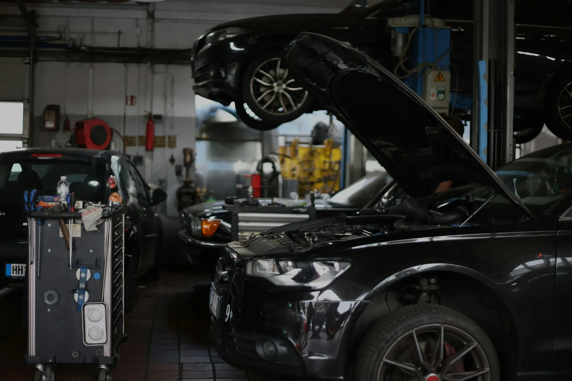 Repair shop interior with a dark sedan on a lift and its hood open